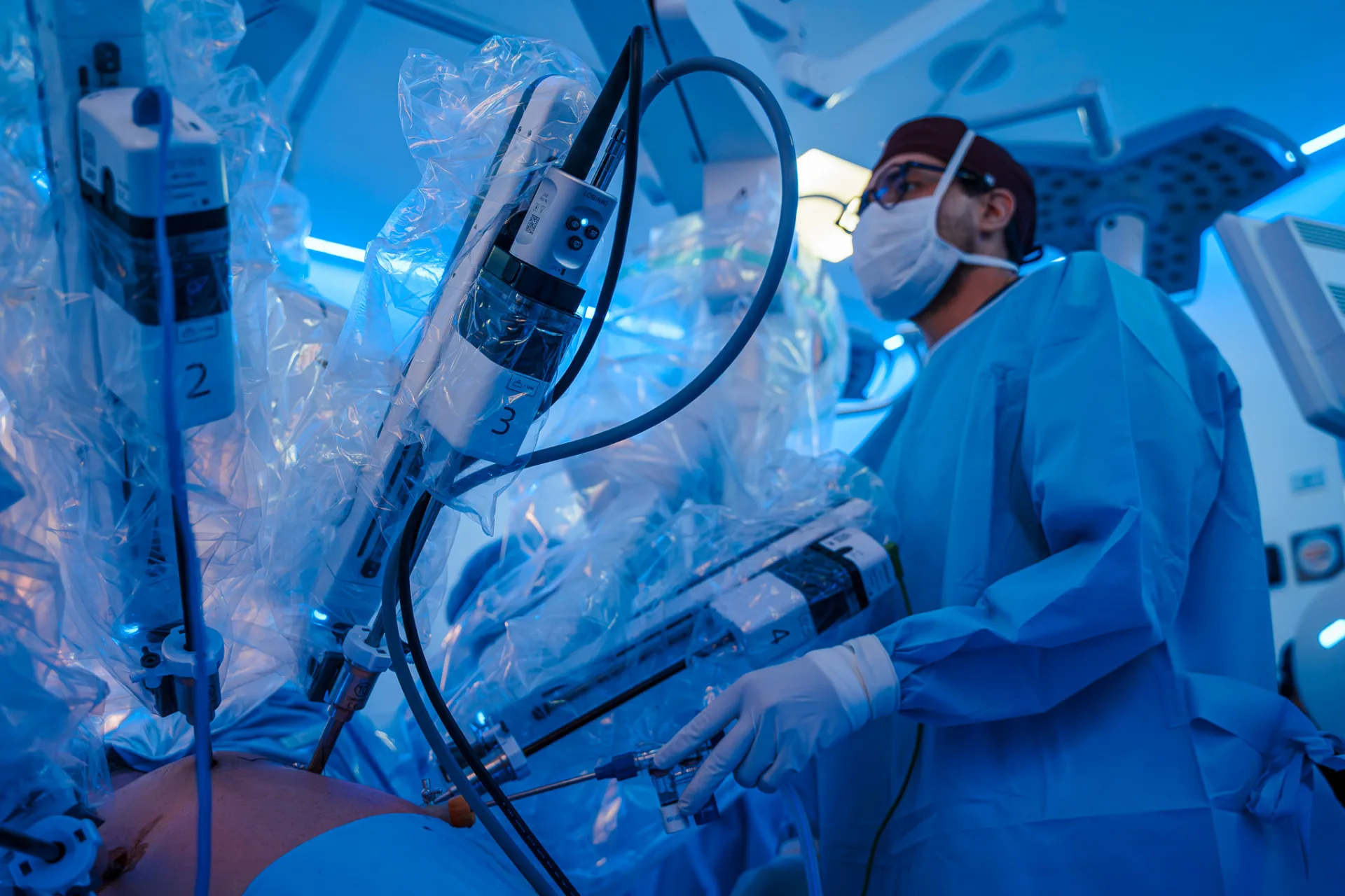 Surgeon in gown, mask and cap adjusting a sterile-draped OMNIBOT MP 1000 robotic arm in a blue-lit operating room